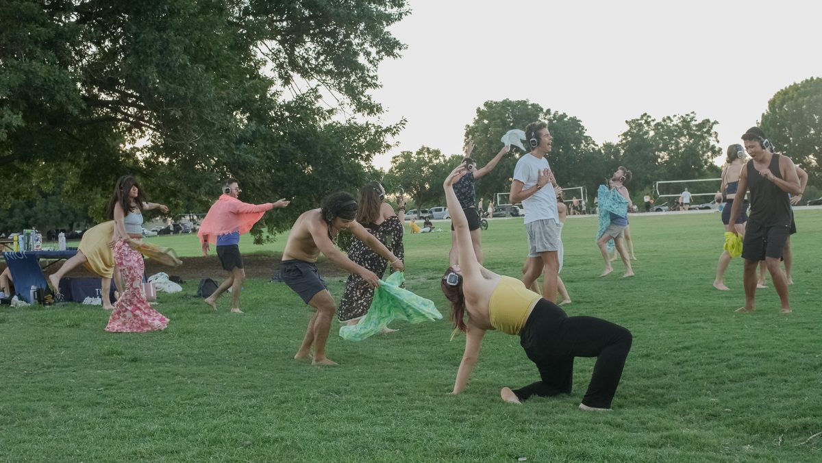 Silent disco in an Austin park at sunset, dancers in wireless LED headphones